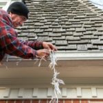 Man in Plaid Shirt on Ladder Hanging Christmas Lights on House